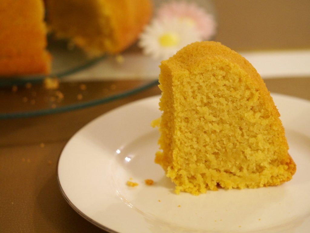 Ein Stück des Gugelhupf auf einem Kuchenteller, dahinter der angeschnittene Kuchen