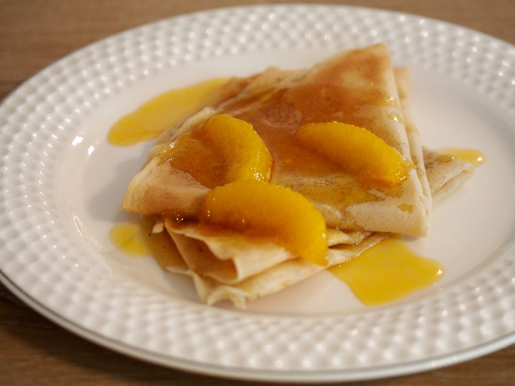 Ein paar Crepes mit Orangenfilets auf einem Teller
