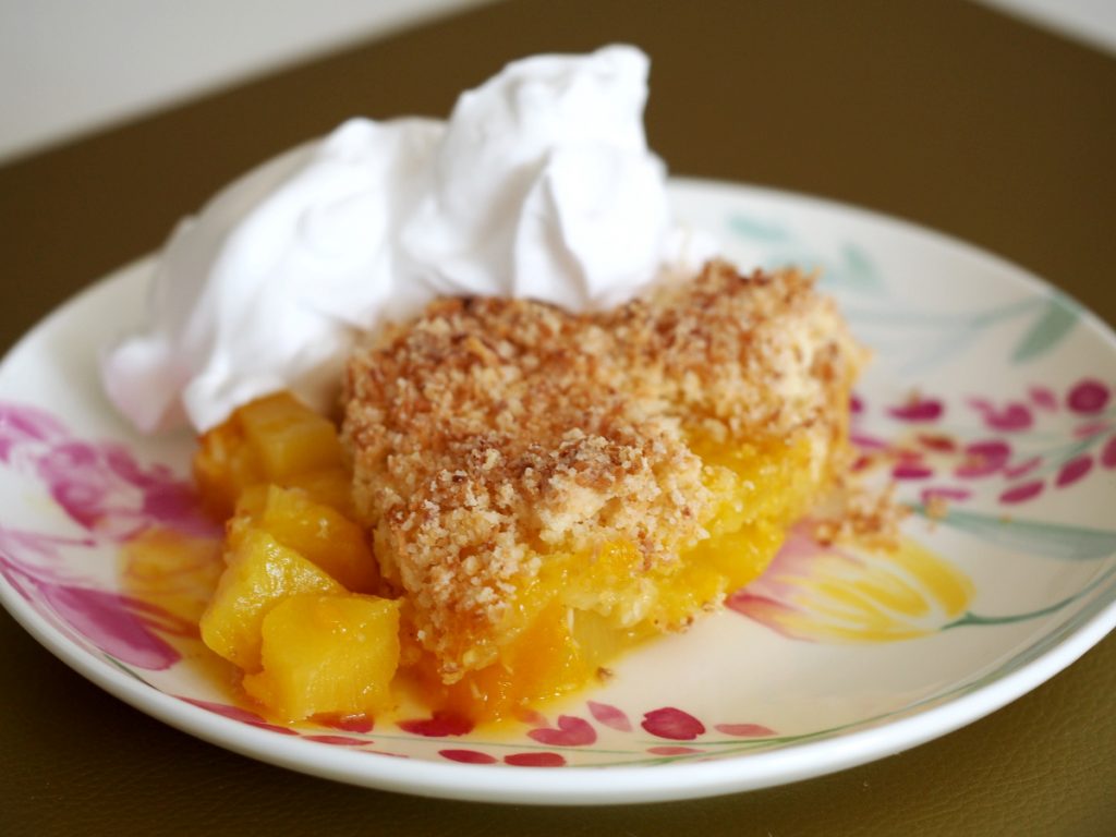 Ein Ananas-Crumble auf einem Teller mit etwas aufgeschlagener veganer Sahne daneben
