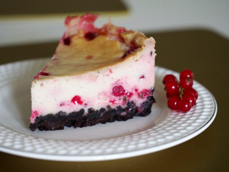 Ein Stück eines Cheesecake mit roten Johannisbeeren und Oreo-Keks Boden
