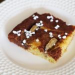 Ein Marmorkuchen mit Bananen vom Blech. Ein Stück, dekoriert mit etwas Hagelzucker liegt auf einem Teller.