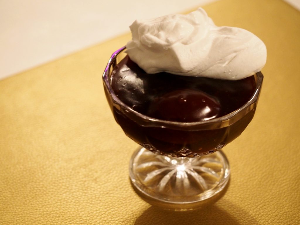 Eine Dessertschüssel mit etwas Rotwein-Pflaumen-Pudding und etwas Sahne darauf