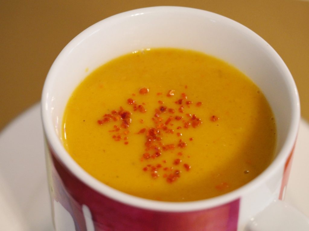 Eine Kürbissuppe, garniert mit ein paar Chiliflocken in einer bunten Jumbotasse
