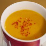 Eine Kürbissuppe, garniert mit ein paar Chiliflocken in einer bunten Jumbotasse