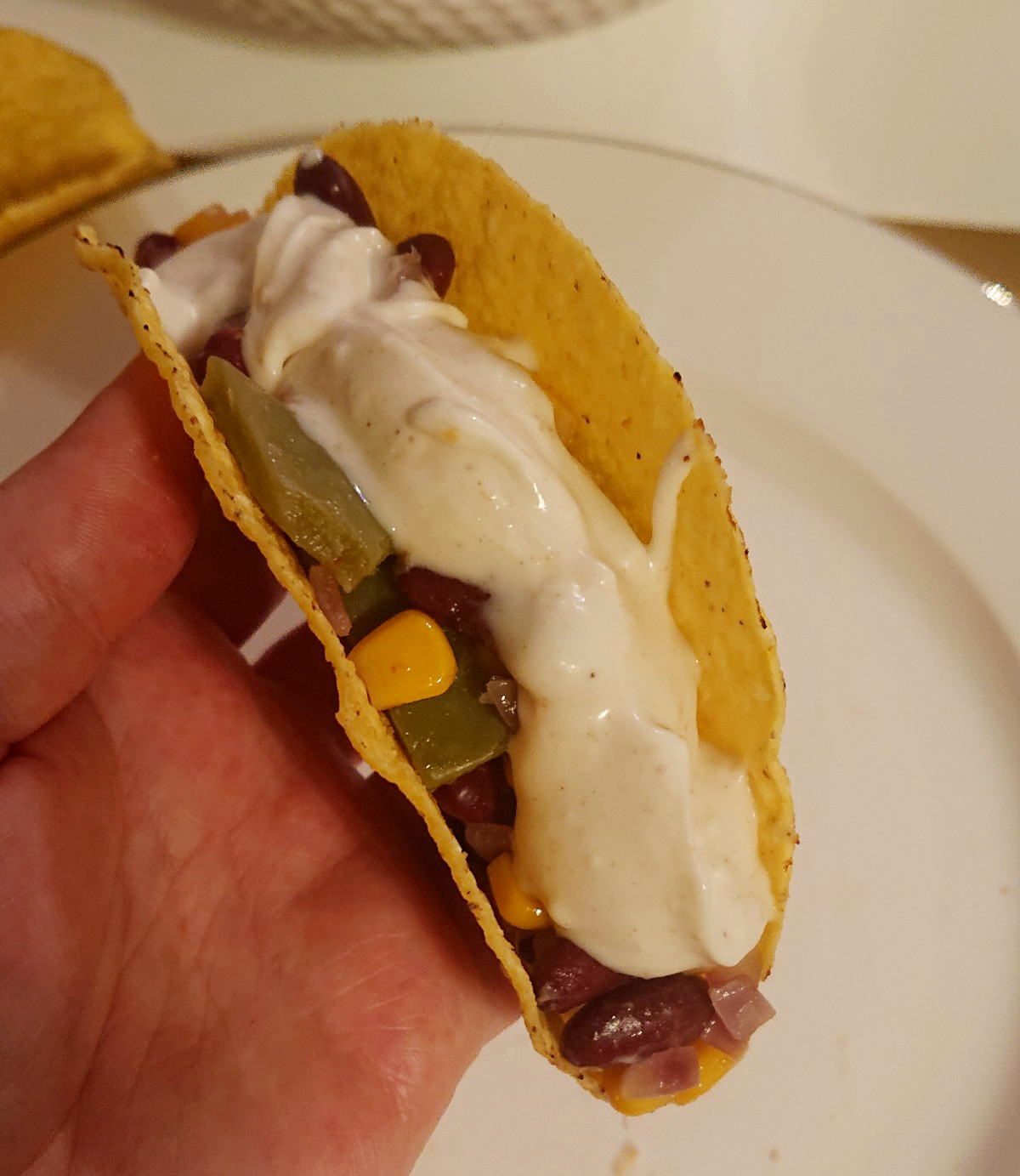 Ein Taco in der Hand gefüllt mit Nopales, Mais, Kidneybohnen und dem Dip