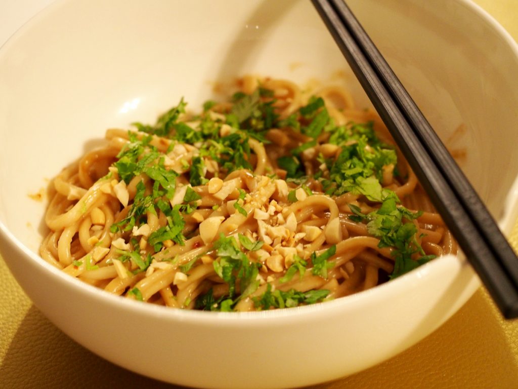 Udon mit Erdnusssauce in einer Schüssel, dekoriert mit klein geschnittener Frühlingszwiebel