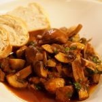 Ein Pilzgulasch in einer Schüssel. Am Rand liegen ein paar kleine Brotscheiben