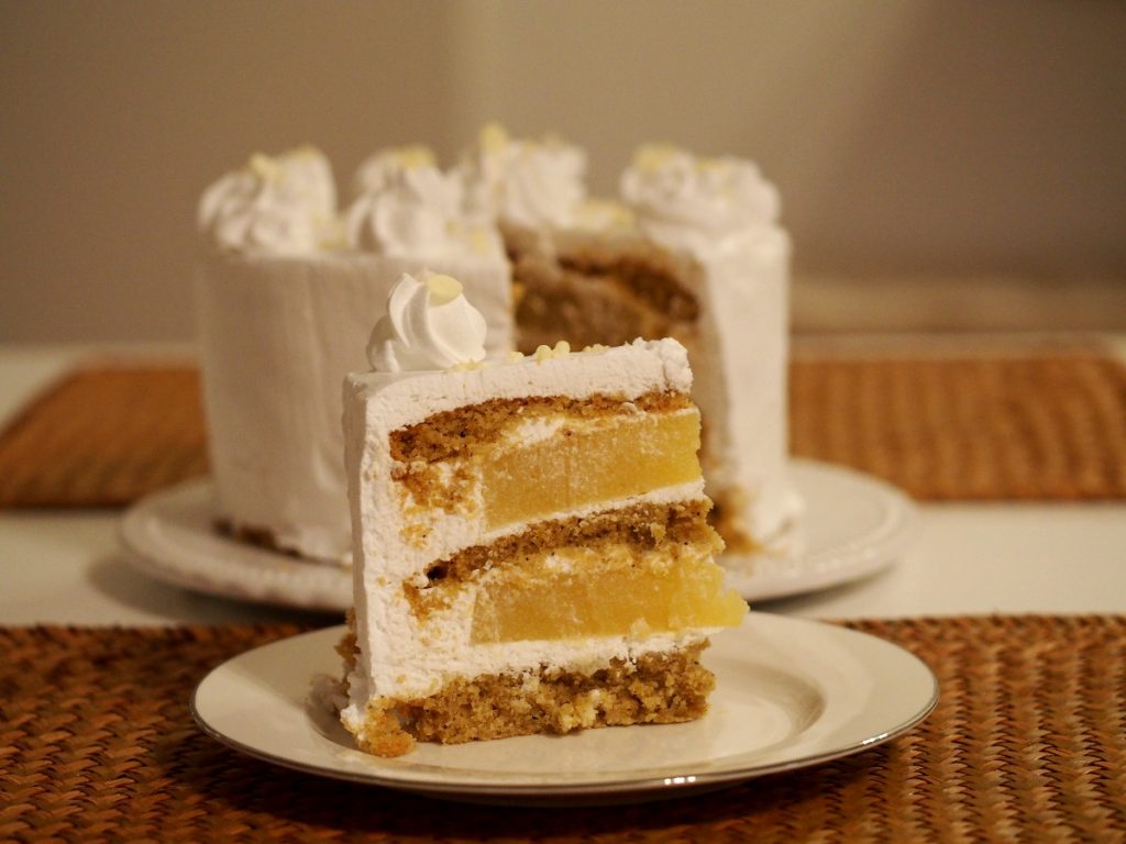 Ein Stück der Ananas-Torte im Vordergrund, dahinter die angeschnittene Torte