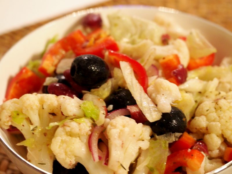 Eine kleine Schüssel mit einem Salat aus Blumenkohl, Paprika und Oliven