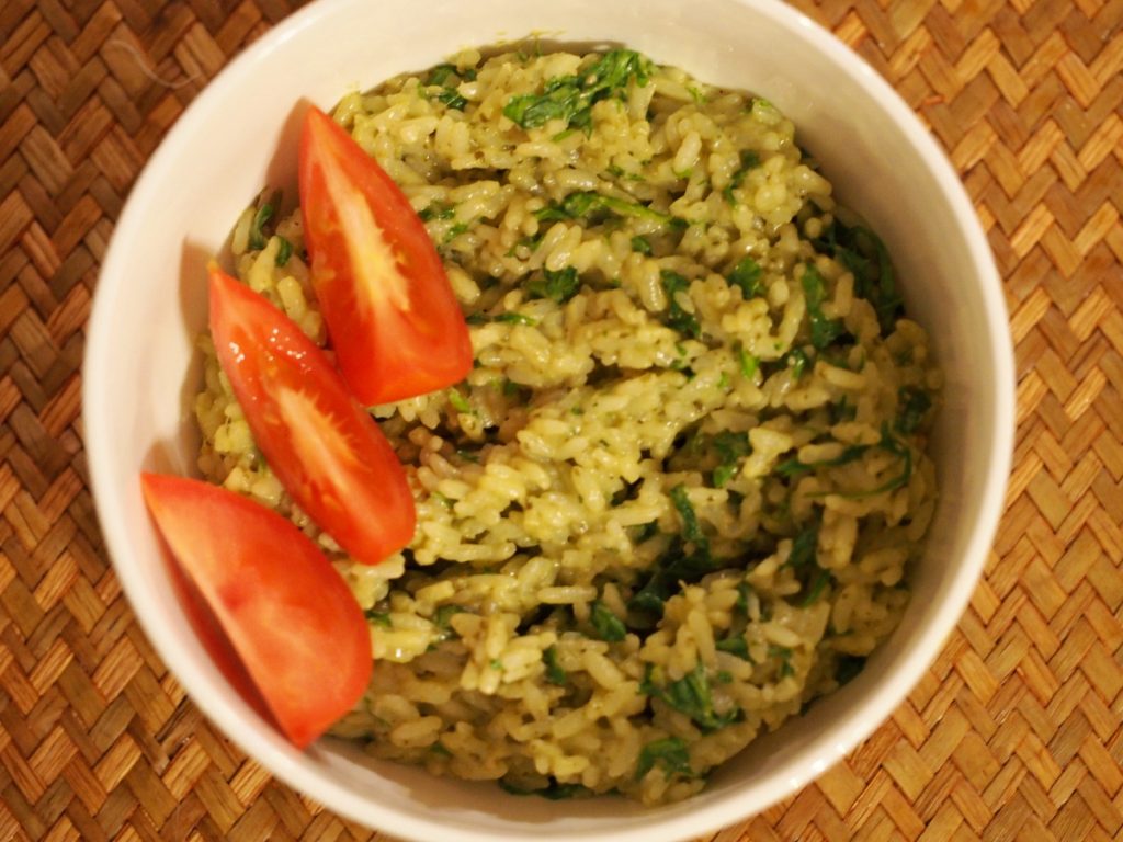 Reis mit Rucola und Pesto in einer Schüssel, darauf ein paar Tomatenspalten