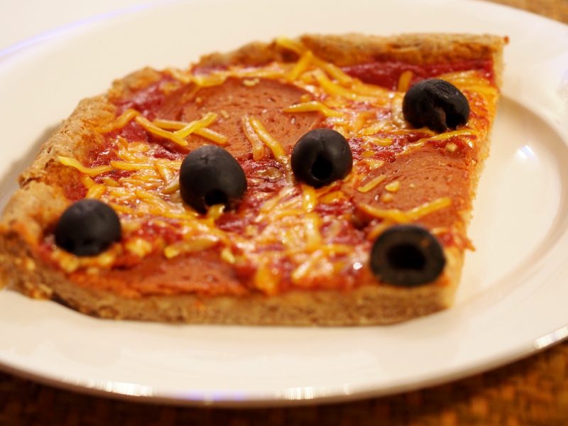 Ein Stück einer veganen Salamipizza auf einem Teller