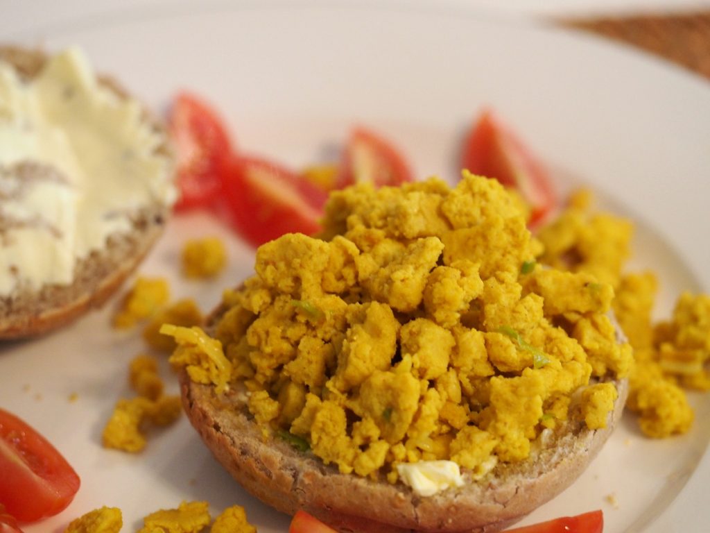 Ein Haufen Rührtofu auf einem mit Margarine bestrichenen halben Brötchen