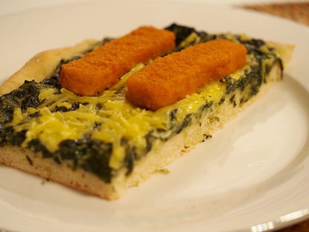 Ein Stück einer Spinatpizza mit veganen Fischstäbchen