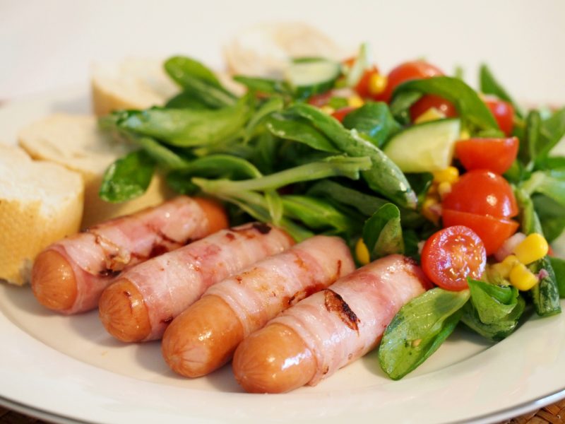 Gebratene Mini-Berner Würstchen neben grünem Salat und aufgeschnittenem Baguette