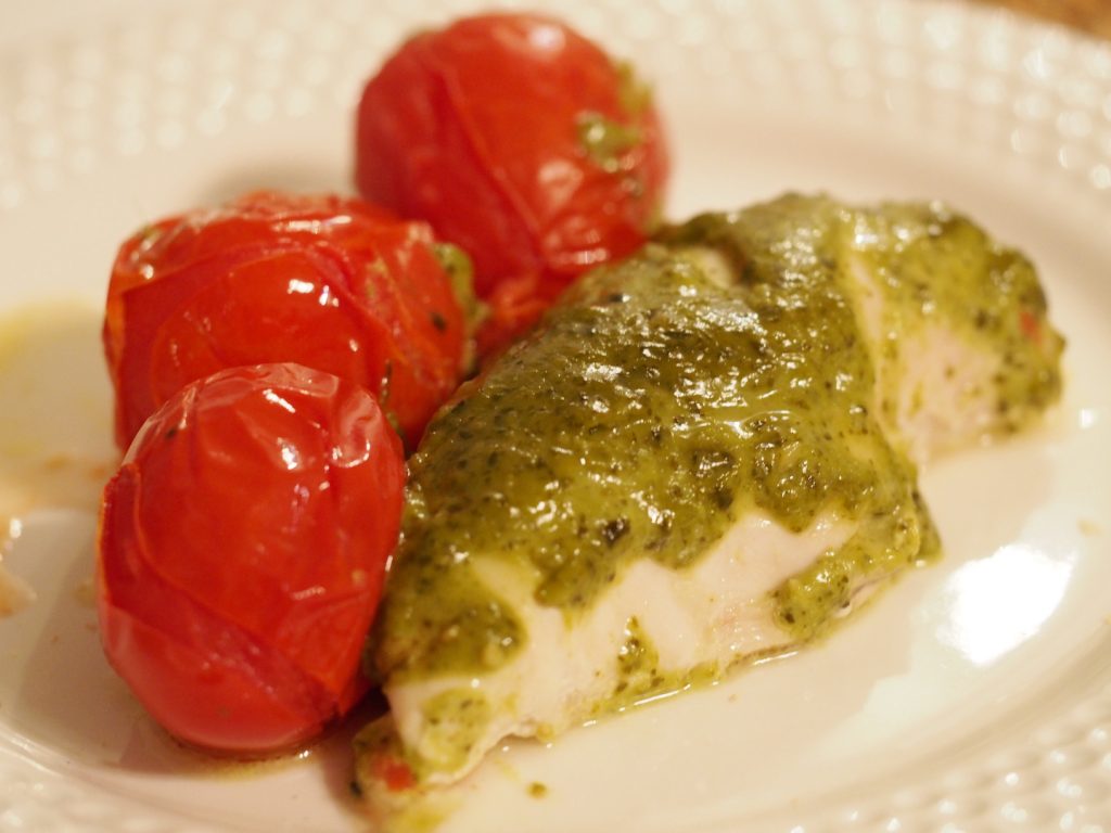 Eine Hühnchenbrust gegart mit Pesto, daneben ein paar im Ofen gegarte kleine Tomaten