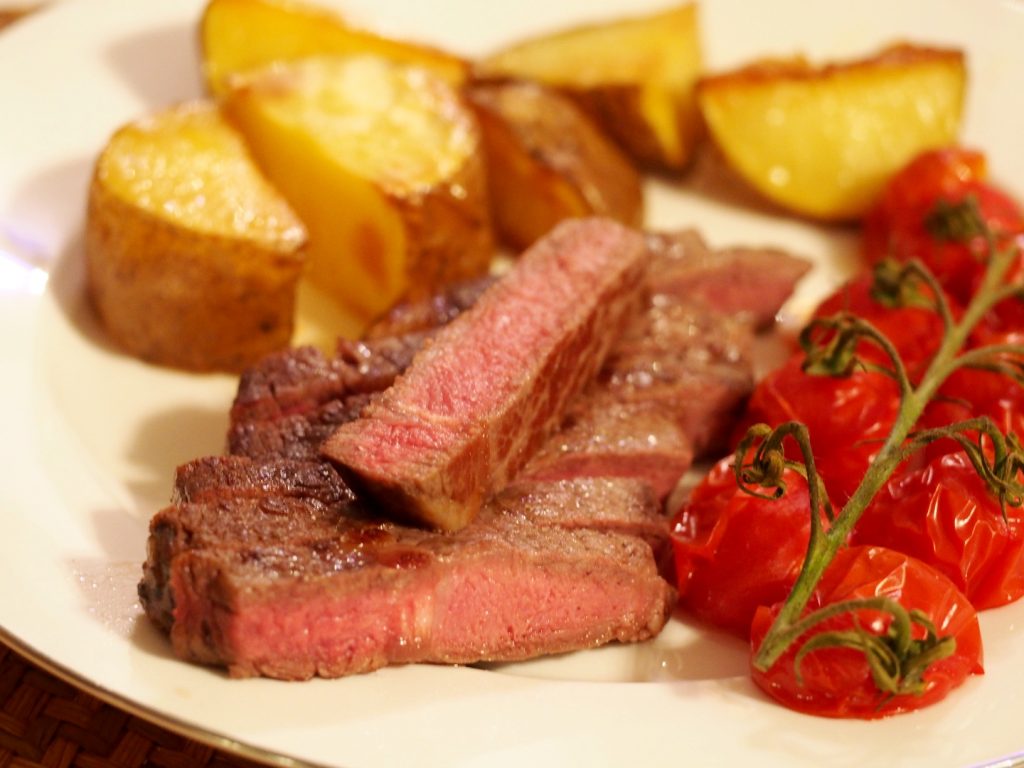 Ein aufgeschnittenes Ribeye Steak mit gebackenen Kartoffeln und Tomaten