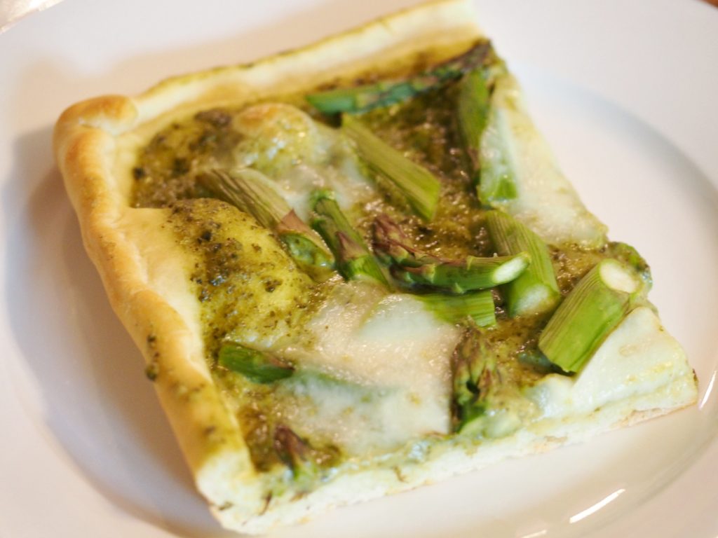 Ein Stück Pizza mit Pesto, Mozzarella und grünem Spargel
