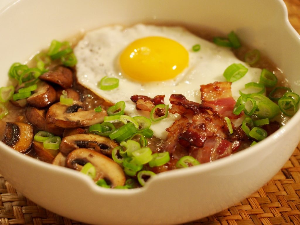 Ein asiatisches Congee mit Ei, gebratenem Speck und gebratenen Champignons