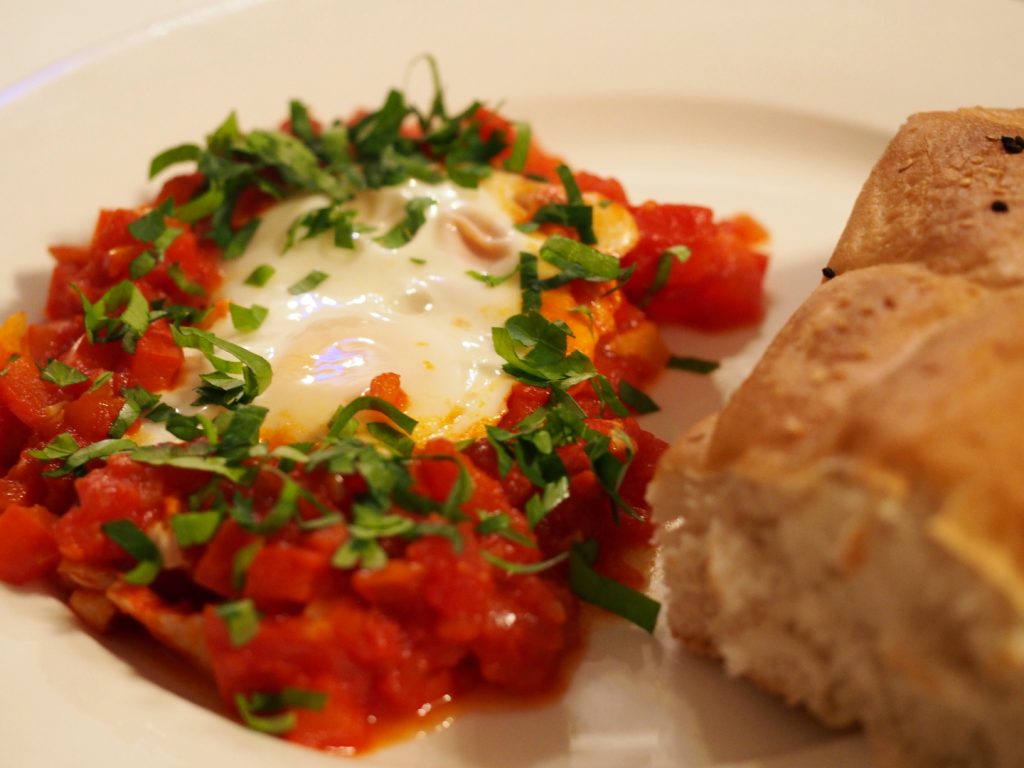 Eine Portion der Shakshuka neben einem Stück Brot