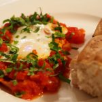 Eine Portion der Shakshuka neben einem Stück Brot