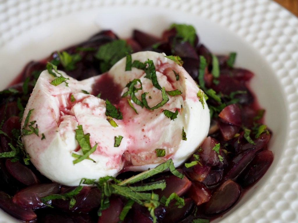 Ein aufgeschnittener Burrata auf marinierten roten Trauben