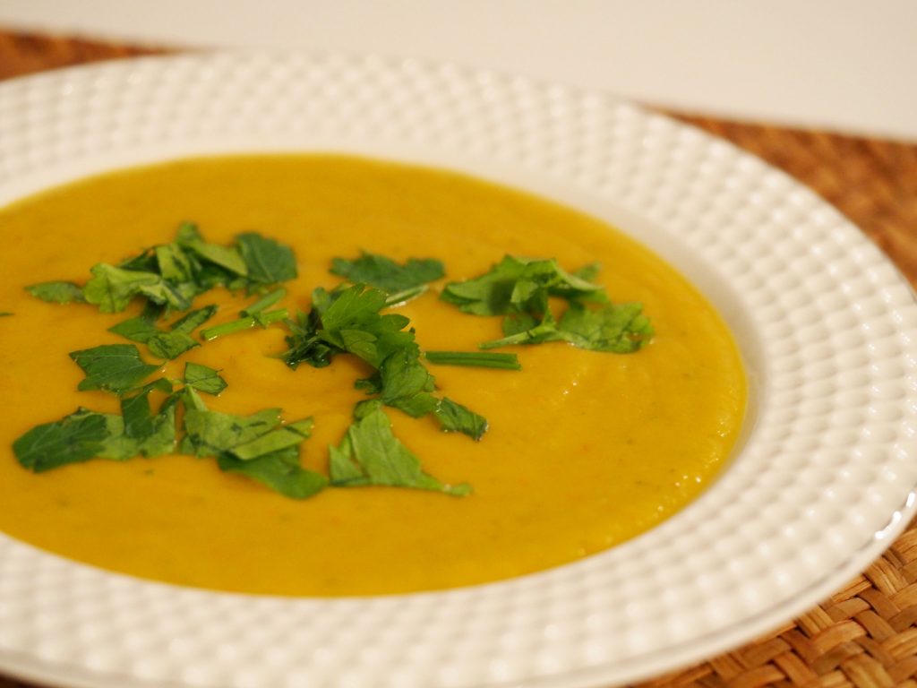 Ein Teller veganer Kürbissuppe, dekoriert mit frischen Kräutern