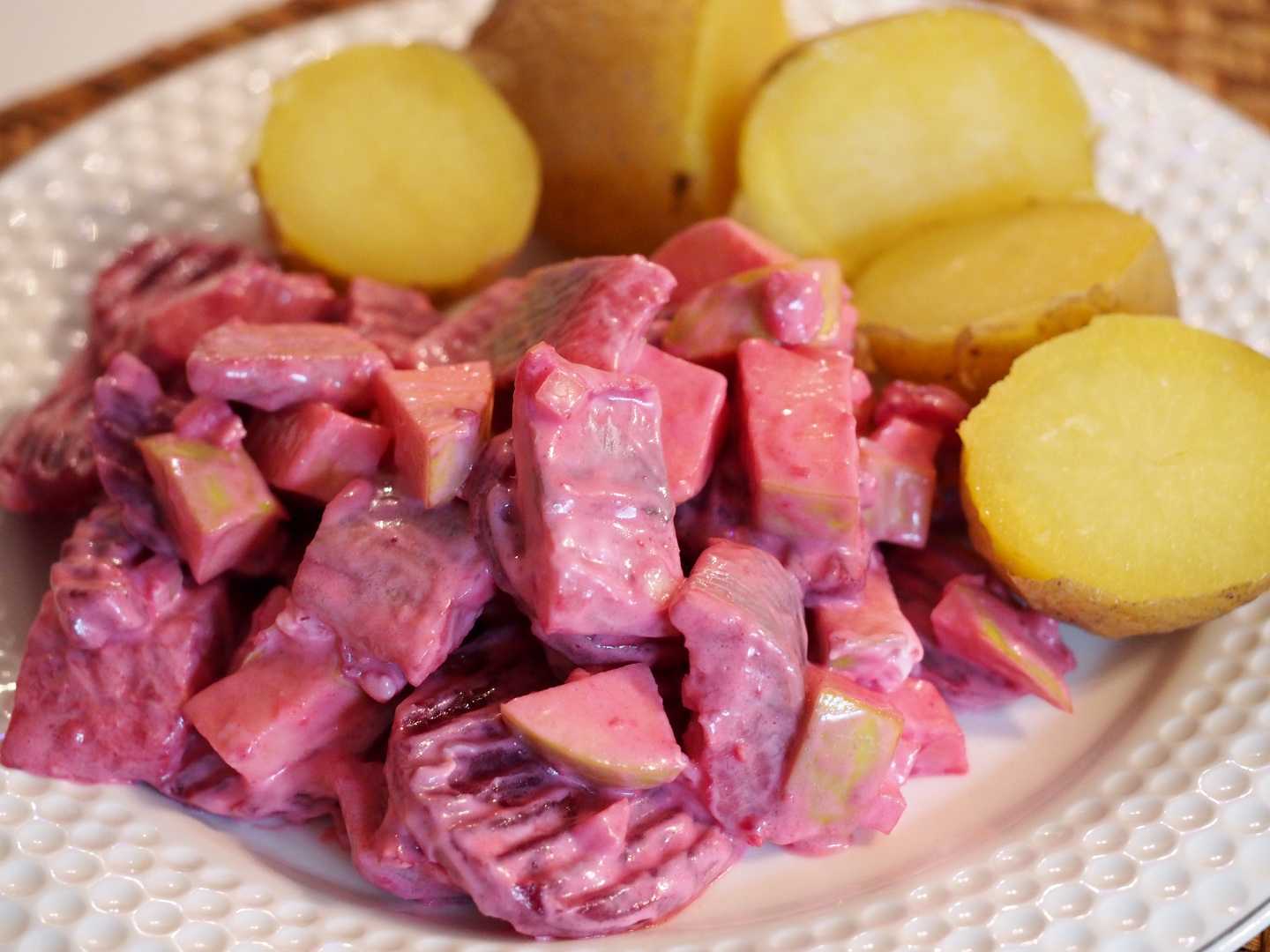Ein frischer und rosa farbener Matjessalat mit roter Bete auf einem Teller neben ein paar gekochten Kartoffeln