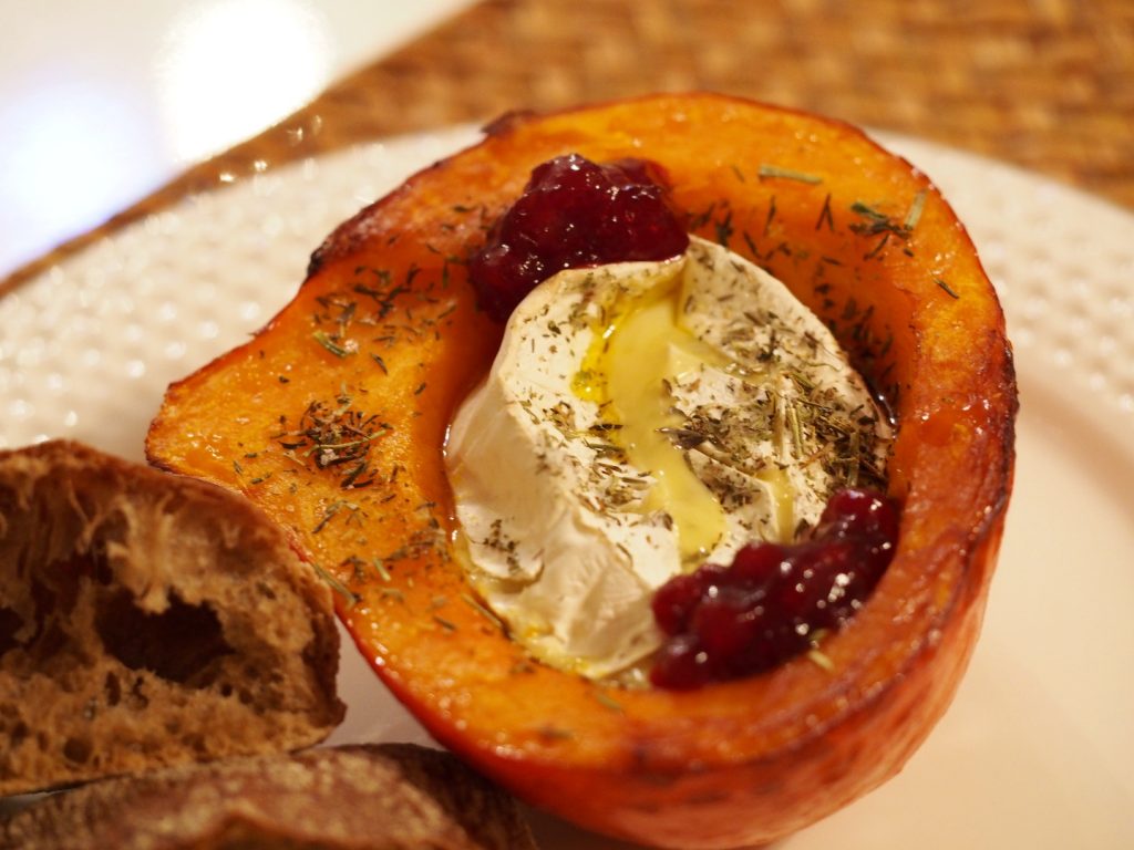 Ein in einer Kürbishälfte gebackener Camembert mit etwas Preiselbeeren an der Seite der Aushölung