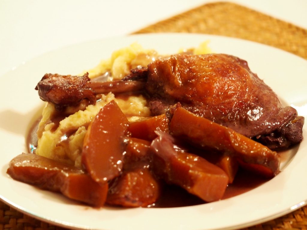 Eine geschmorte Entenkeule in Rotweinsauce neben Kürbisgemüse und Kartoffelstampf