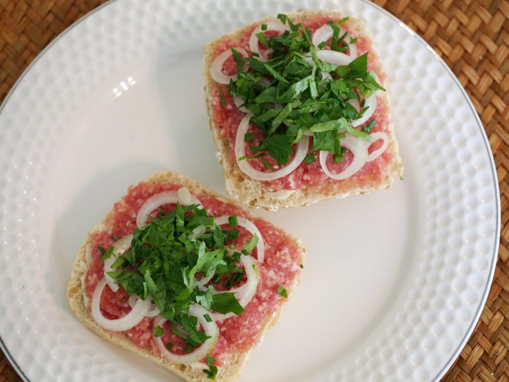 Zwei Brötchenhälften jeweils mit Mett bestrichen und mit Zwiebel und verschiedenen Kräutern belegt