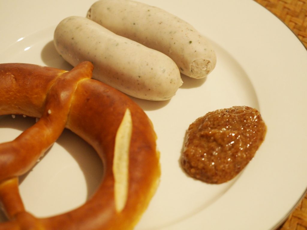 Zwei gebrühte Weißwürste neben einer Brezel und etwas süßem Senf
