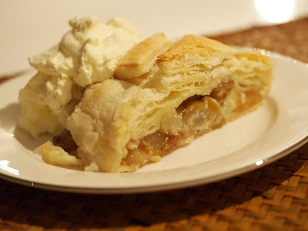 Ein Stück des Birnenstrudels auf einem Teller. Dahinter wurde etwas vegane Sahne drapiert.