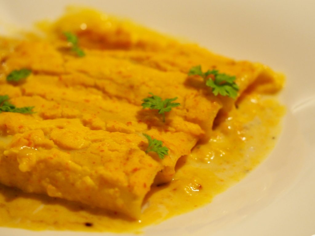 Vier oder fünf mit Kürbissauce gefüllte Cannelloni auf einem Teller.