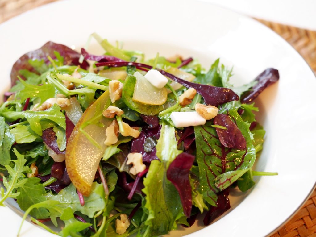 Ein Salat mit unterschiedlichen Blättern mit gegarten Birnenscheiben und Hirtenkäse