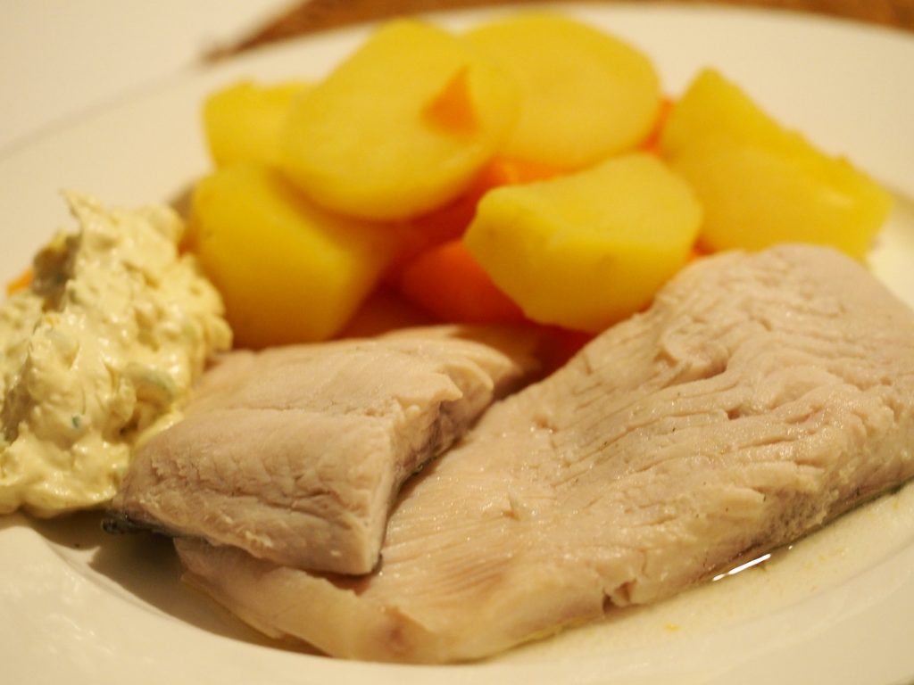 Zwei Stücke Karpfen blau gegart neben einem Dip und gekochten Kartoffeln