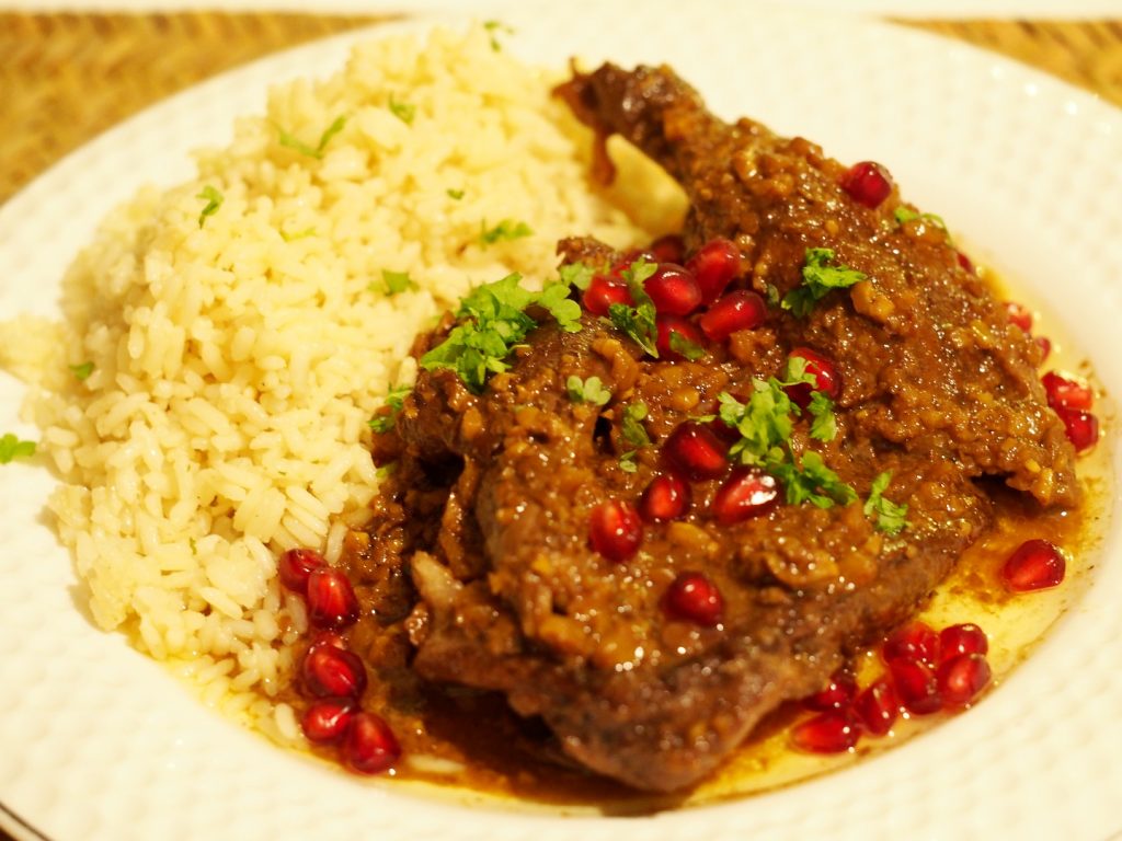Eine geschmorte Entenkeule mit einer Granatapfelsauce neben Reis.