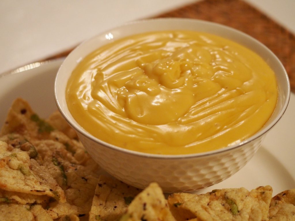 Eine noch unberührte Schüssel des Käsedips neben einem Haufen Nachos