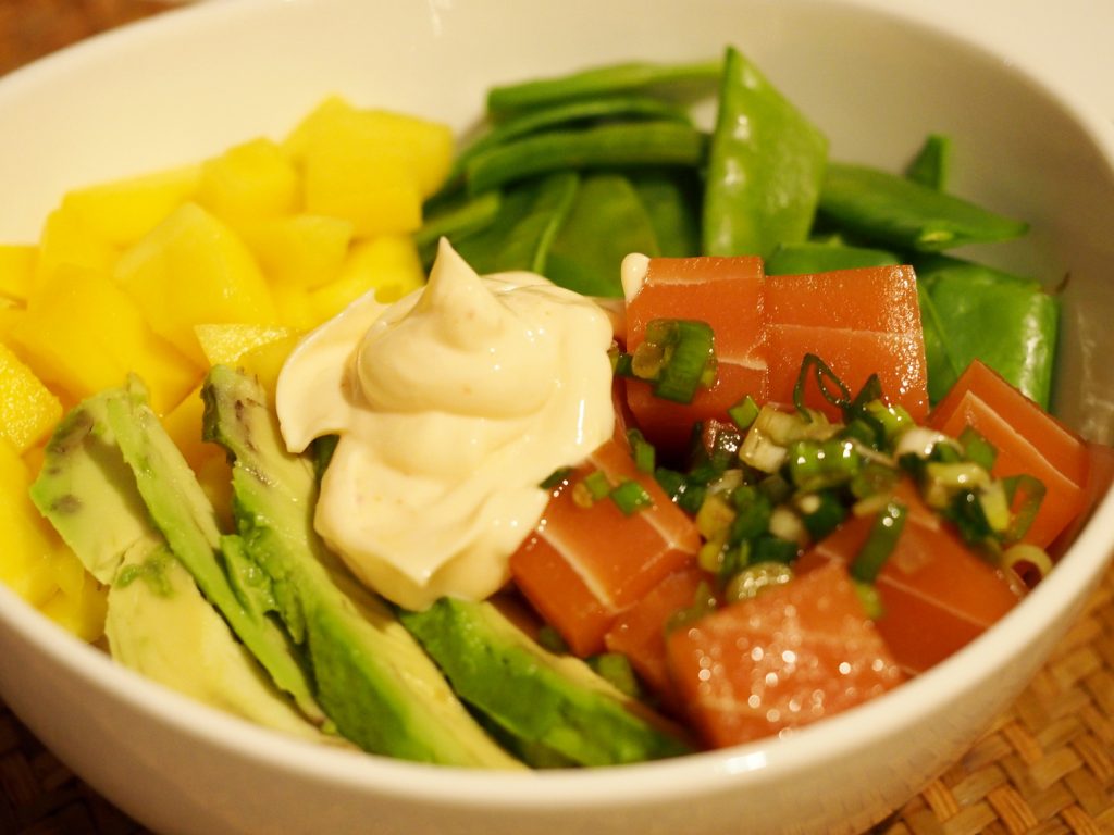 Eine Schüssel gefüllt mit Reis, mariniertem veganen Fisch, Avocado und weiteren Beilagen. In der Mitte ist etwas von der Sauce.