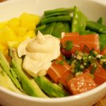 Eine Schüssel gefüllt mit Reis, mariniertem veganen Fisch, Avocado und weiteren Beilagen. In der Mitte ist etwas von der Sauce.
