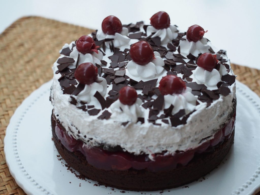 Die ganze Torte auf einer Tortenplatte. Die Stückgrößen sind jeweils mit einem Cremetuff und einer Kirsche markiert und dekoriert.