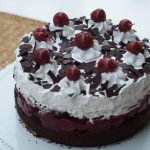 Die ganze Torte auf einer Tortenplatte. Die Stückgrößen sind jeweils mit einem Cremetuff und einer Kirsche markiert und dekoriert.