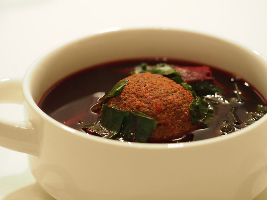 Eine klare rote Bete Suppe mit einem großen Leberknödel in einer Suppentasse