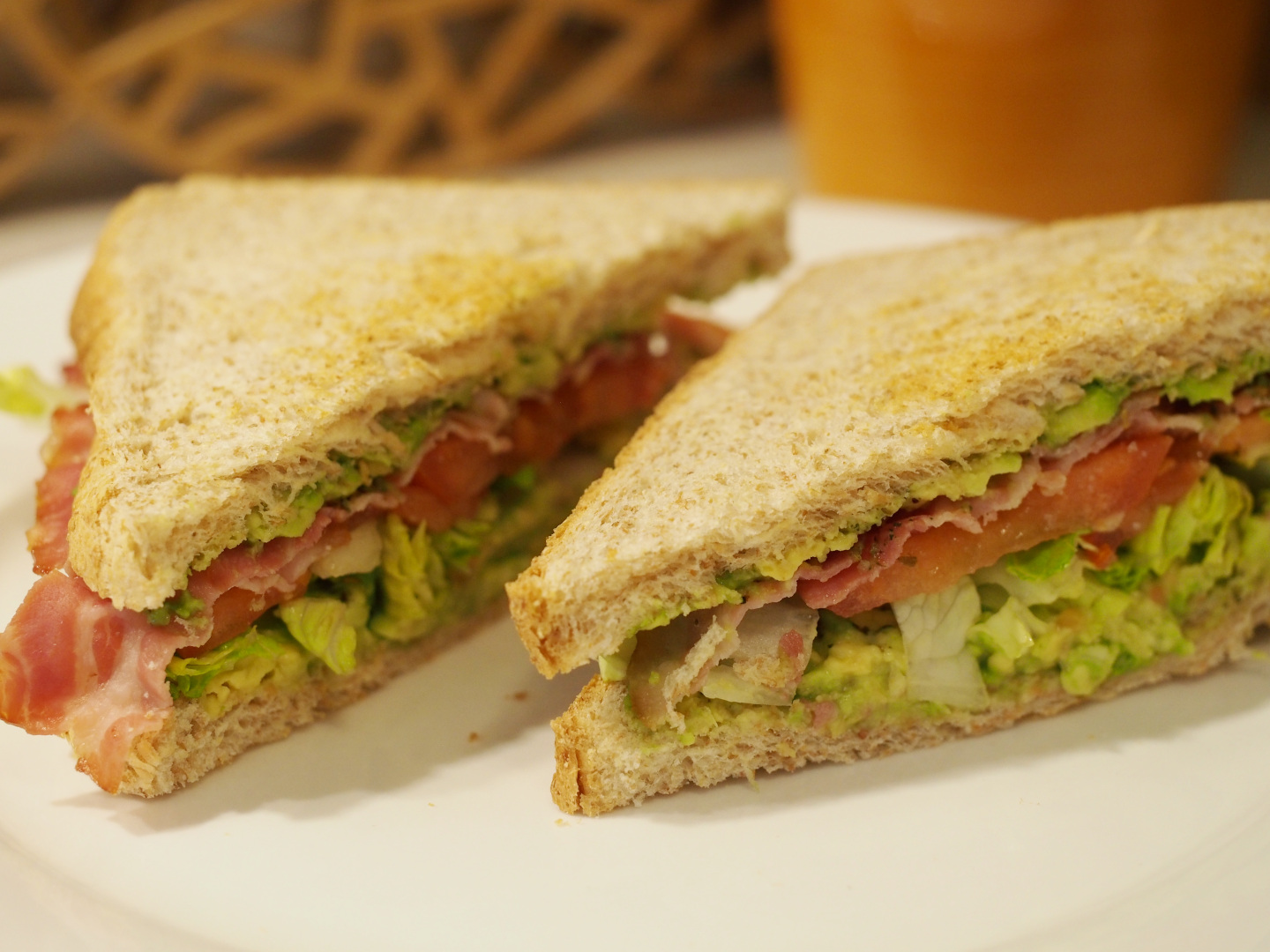 Zwei diagonal aufgeschnittene BLTA-Sandwich Portionen belegt mit Bacon, Salat, Tomate und Avocado zwischen zwei Vollkorntoastscheiben