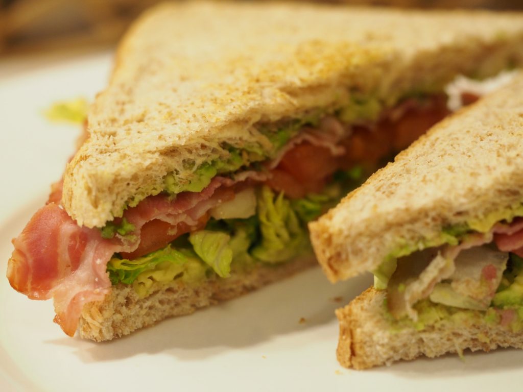 Nahaufnahme des diagonal aufgeschnittenen BLTA-Sandwiches mit Bacon, Salat, Tomate und Avocado zwischen zwei Vollkorntoastscheiben