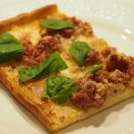 Ein Stück der Pizza Bianca belegt mit viel Mozzarella, Salsiccia und frischem Basilikum