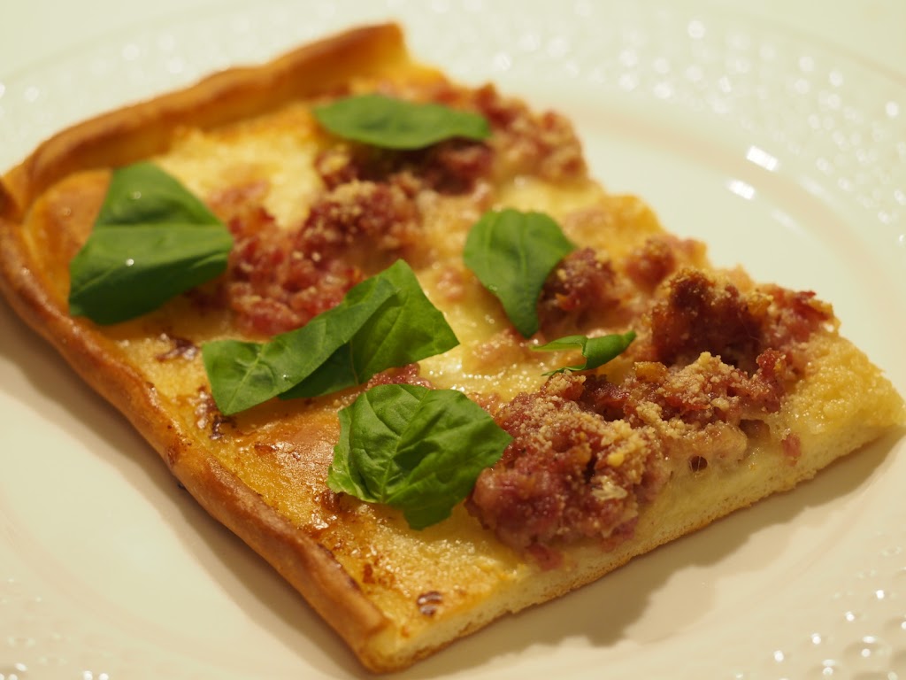 Ein Stück der Pizza Bianca belegt mit viel Mozzarella, Salsiccia und frischem Basilikum