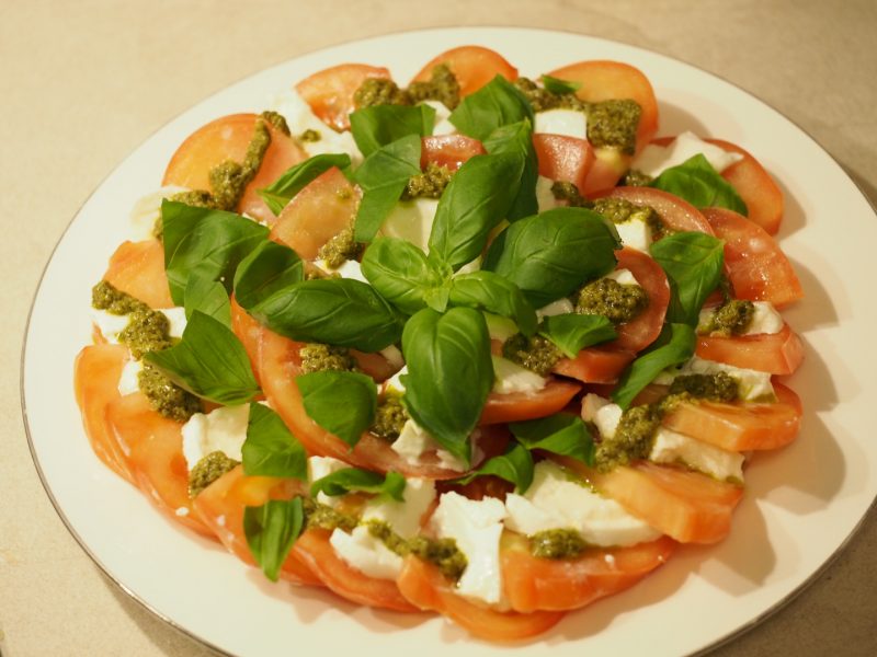 Ein großer Teller mit Cprese Salat aus Tomaten, Mozzarella, Pesto und frischem Basilikum