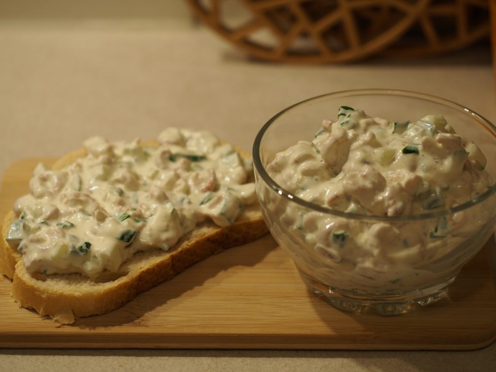 Eine kleine Schüssel gefüllt mit dem Krabbensalat neben einem Brot, das mit dem Krabbensalat belegt wurde.