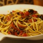 Eine Portion Pasta Puttanesca mit Spaghetti und einer einer Sauce aus Sardelle, Kapern, Oliven, Tomaten und frischen Kräutern
