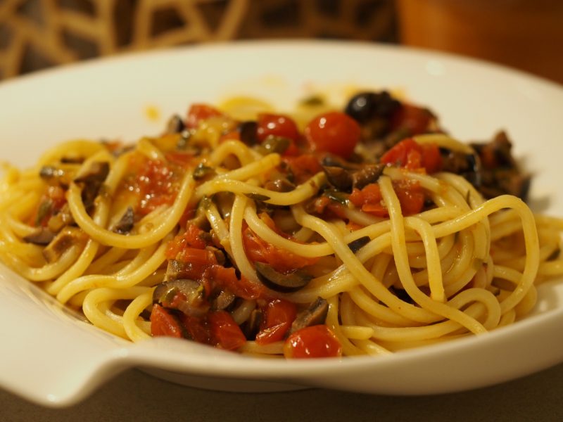 Eine Portion Pasta Puttanesca mit Spaghetti und einer einer Sauce aus Sardelle, Kapern, Oliven, Tomaten und frischen Kräutern